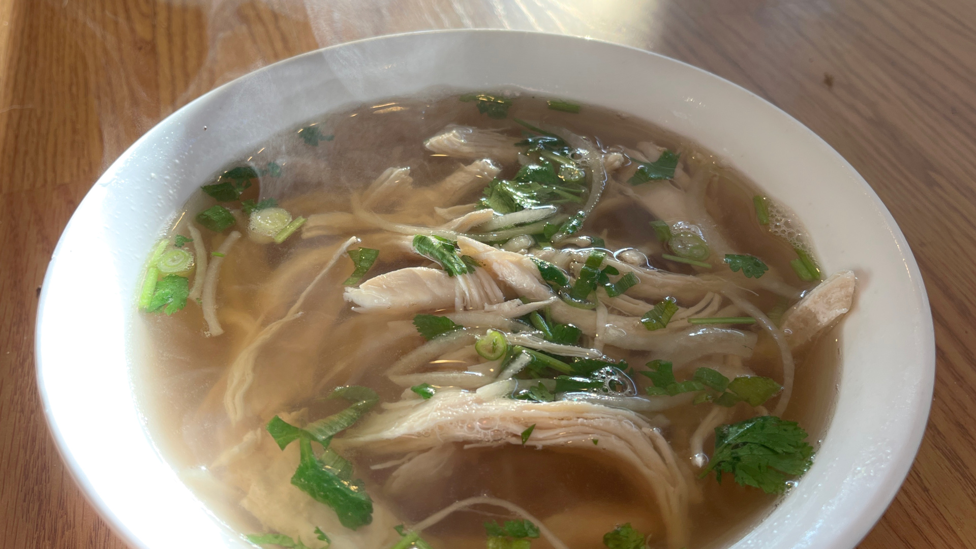 Steaming chicken pho with tender shredded chicken, clear broth, and fresh herbs on a wooden table