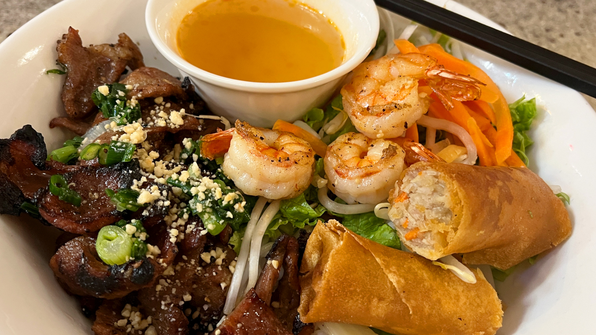 Grilled pork and shrimp vermicelli bowl with fresh vegetables, egg roll, and house dipping sauce