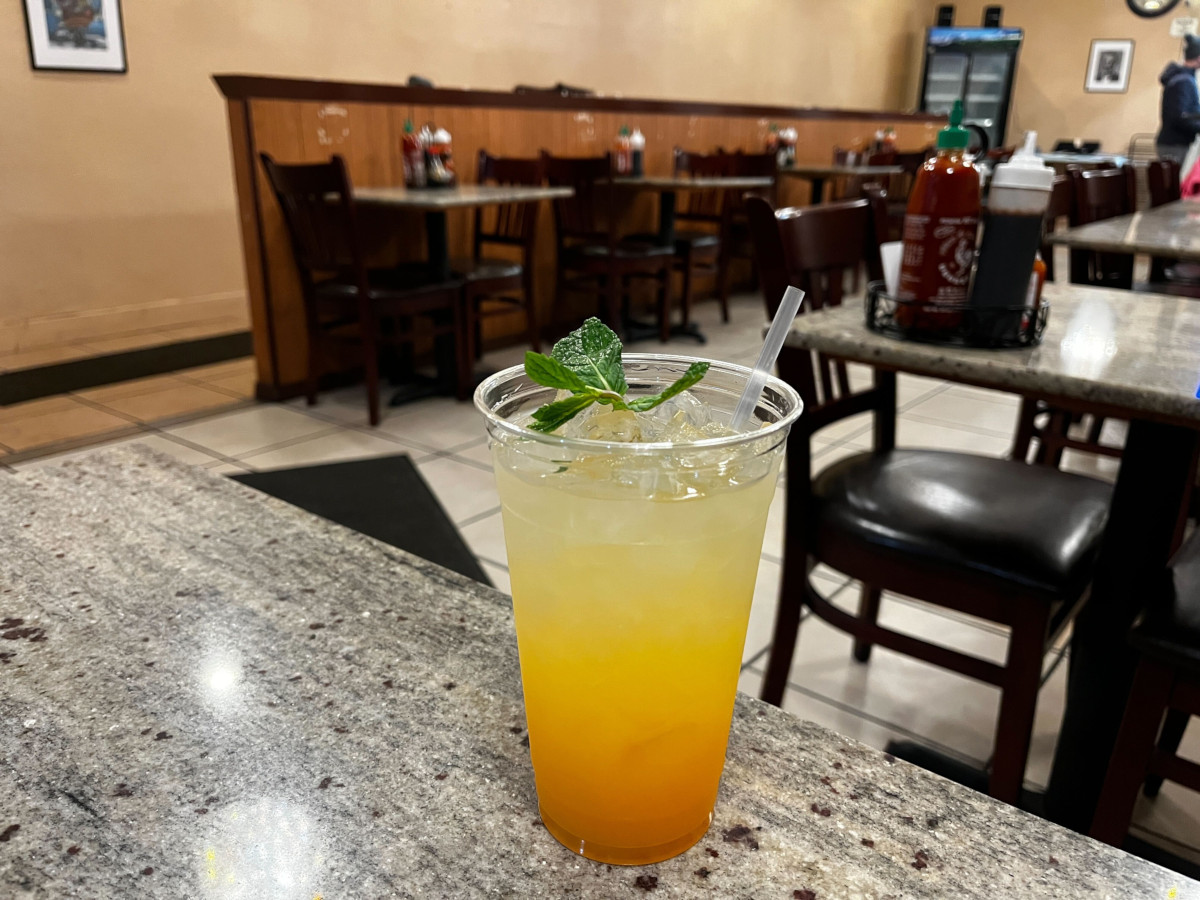 A refreshing glass of Orangiene, a signature triple-citrus house drink with a vibrant orange gradient and fresh mint garnish, served on a granite tabletop at Pho An Restaurant in Seattle.