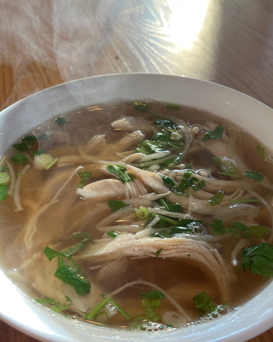 Vietnamese rice noodle soup with chicken breast with steam rising from a white bowl.